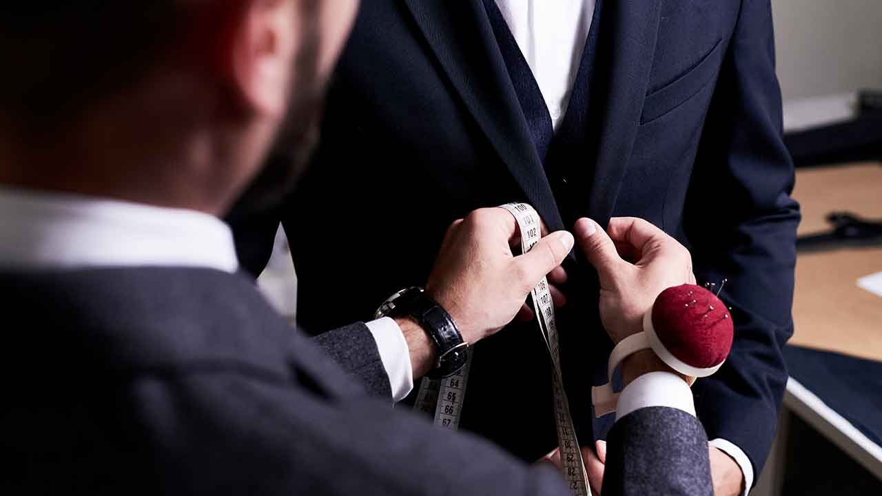 A man in a suit is adjusting a measuring tape.