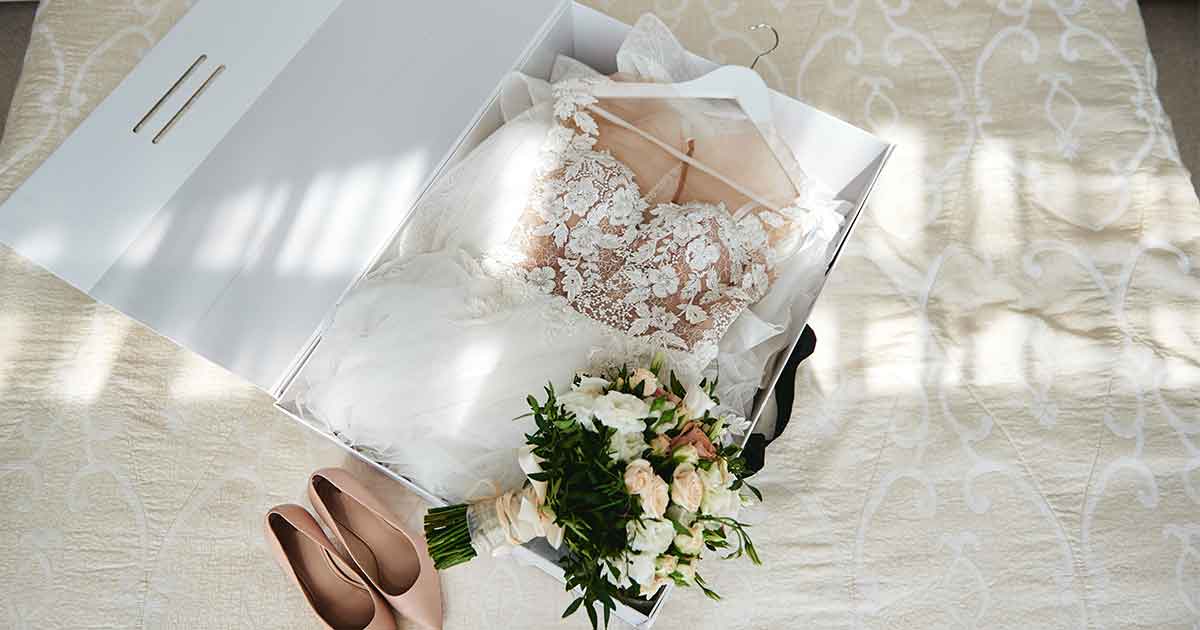 A wedding dress and shoes in a box on a bed.